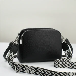 Musta neliönmuotoinen olkalaukku tai Crossbody laukku, jossa on kaksi vetoketjullista osastoa ja leveä mustavalkoinen kuviollinen kangashihna.